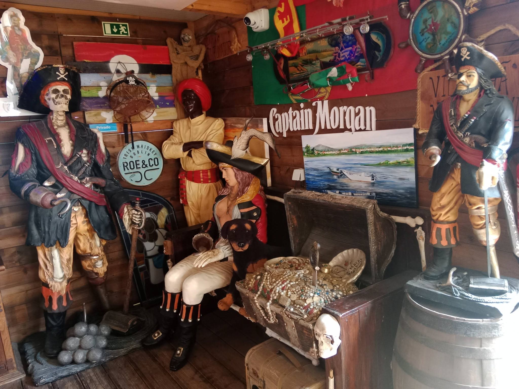 O canto dos piratas em tamanho real, com uma arca a transbordar de colares e moedas, balas de canhão empilhadas e o reclame do Captain Morgan na parede de madeira.