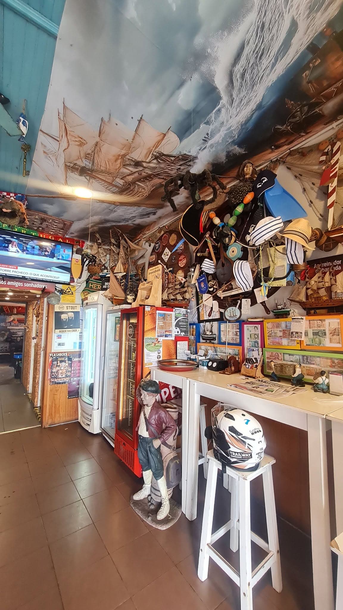 O mural da nau no tecto com uma aranha peluda pendurada a meio, sobre o balcão carregado de chapéus, máscaras de mergulho e barcos de madeira.